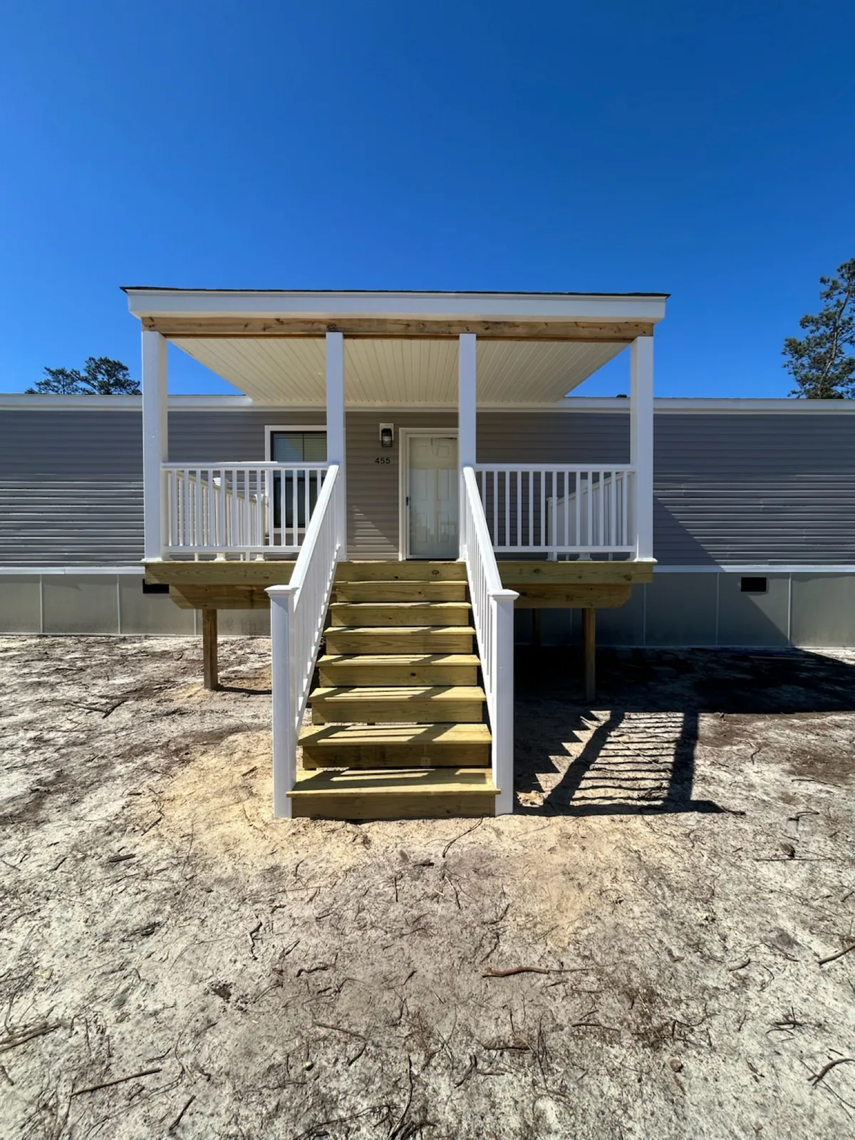 Front view of a covered entry porch with wood stairs and white railings.