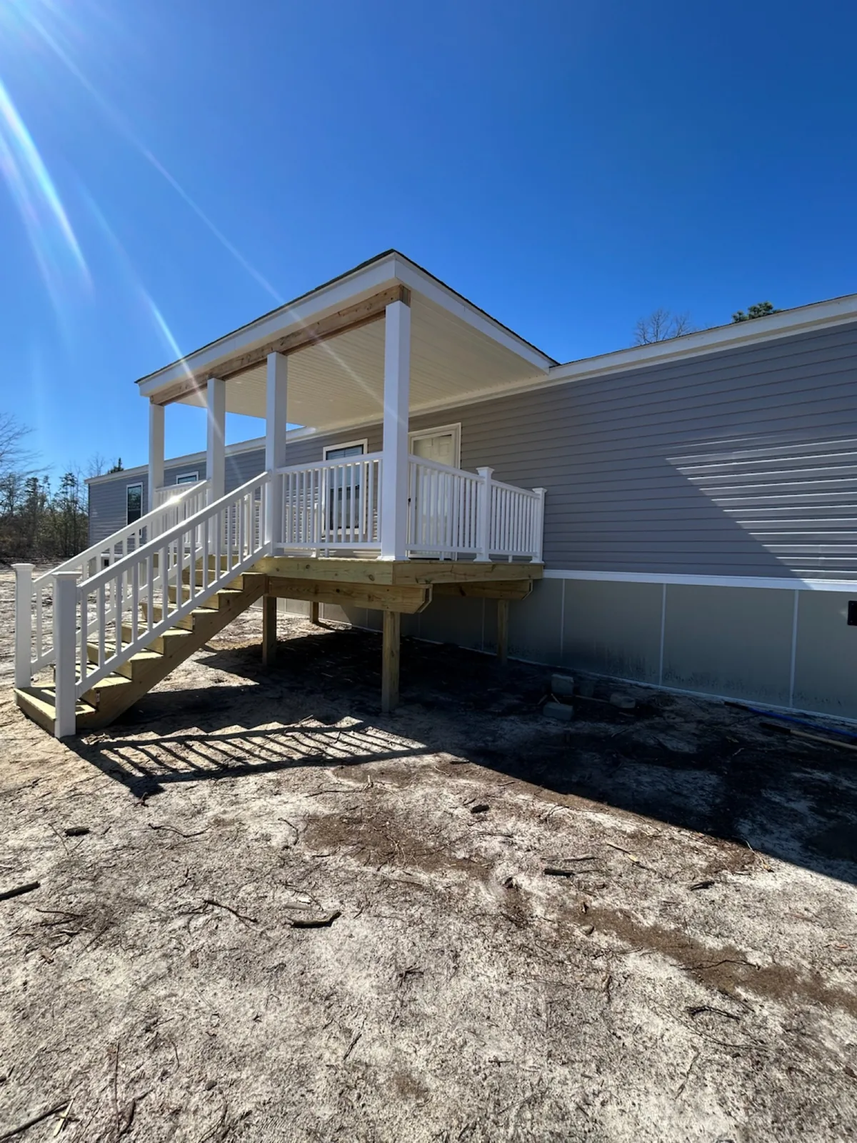 Covered wood entry porch with white railings and stairs beside a manufactured home.