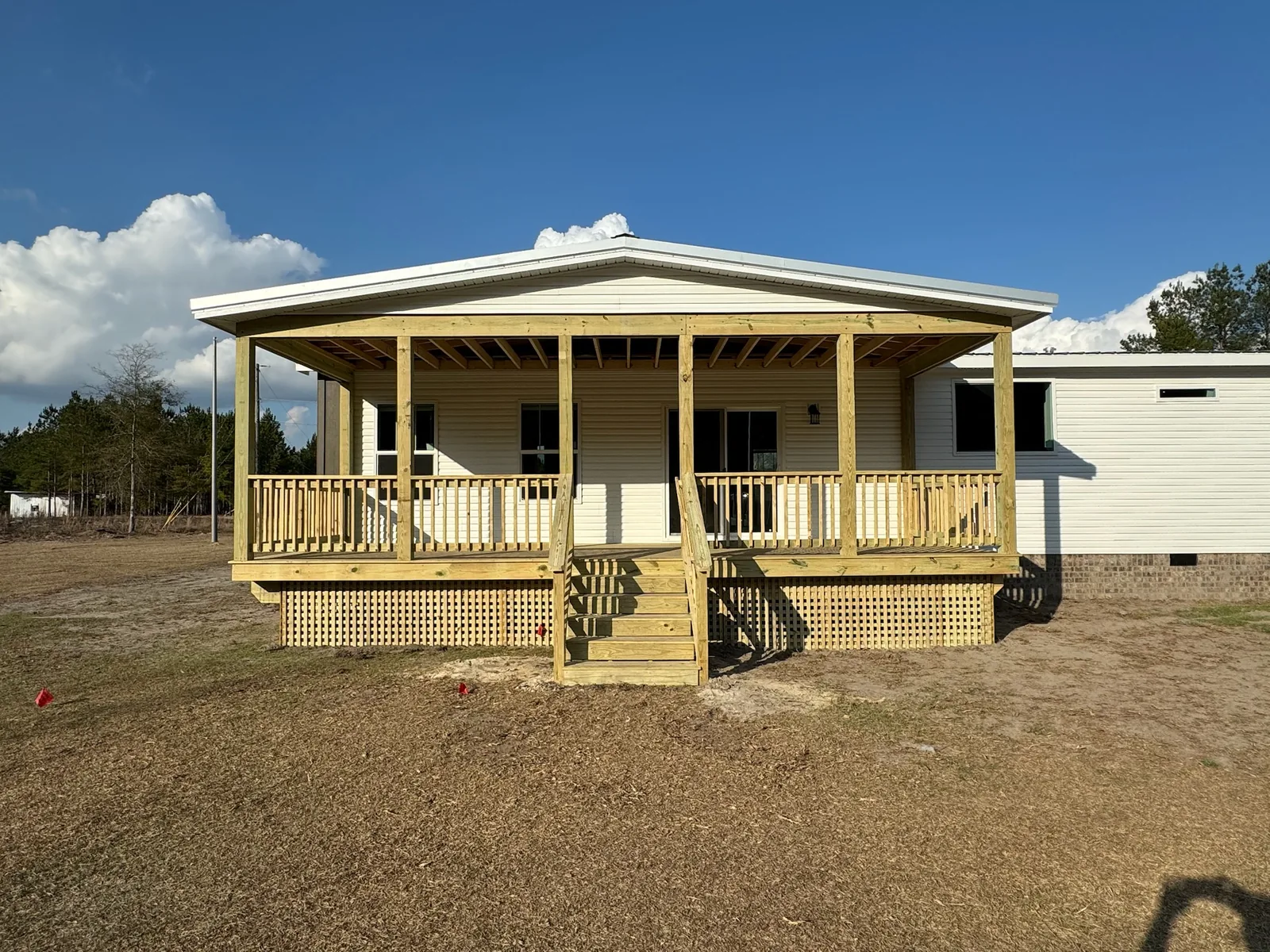 Wide covered wood porch with railings, center stairs, and lattice beneath the deck.