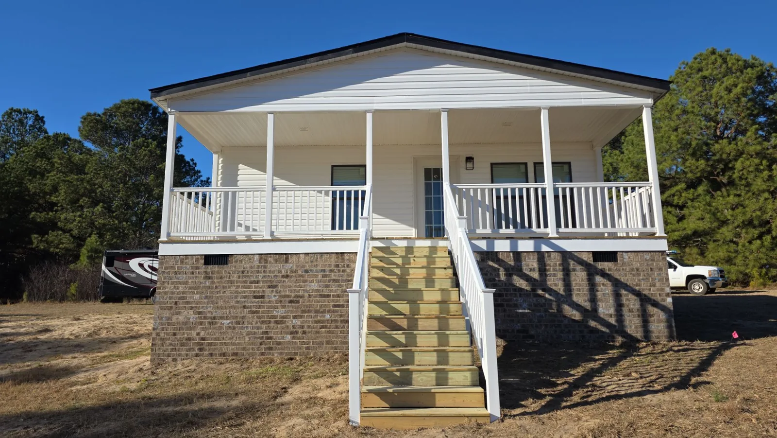 After exterior finishing: the same manufactured home with finished siding, masonry skirting, entry stairs, and white railings.