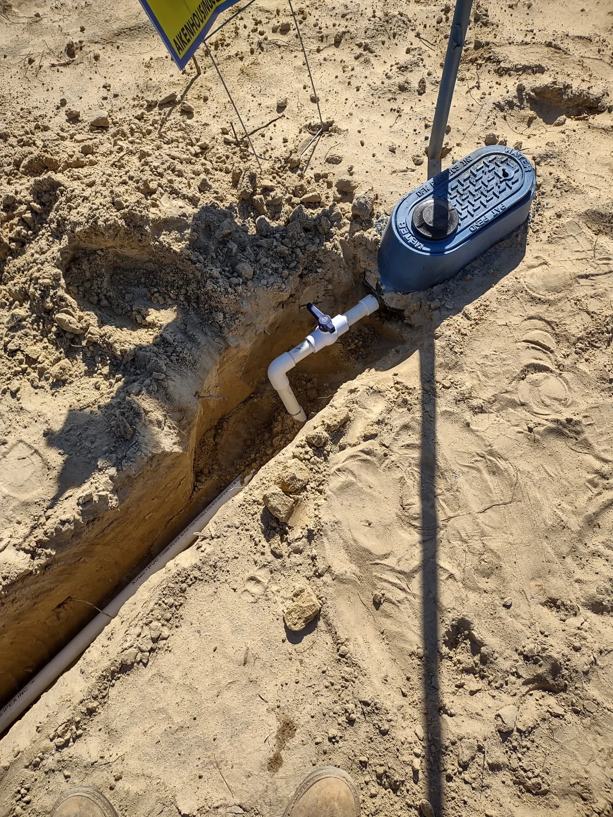 Water meter box, shutoff valve, and service line shown in an open trench during installation.