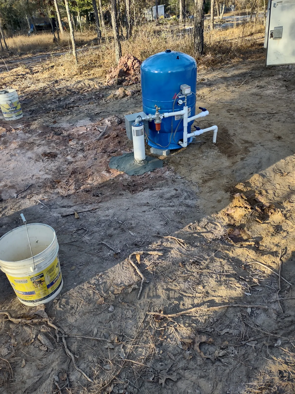 Well pressure tank with connected piping, valves, pressure switch, and well casing.